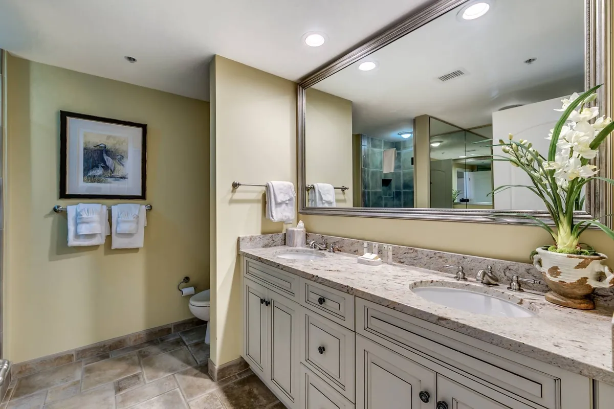 A modern bathroom with a double sink vanity, expansive mirror, and a floral arrangement that adds a welcoming touch. The tranquil setting is perfect for both morning routines and unwinding in the evening.