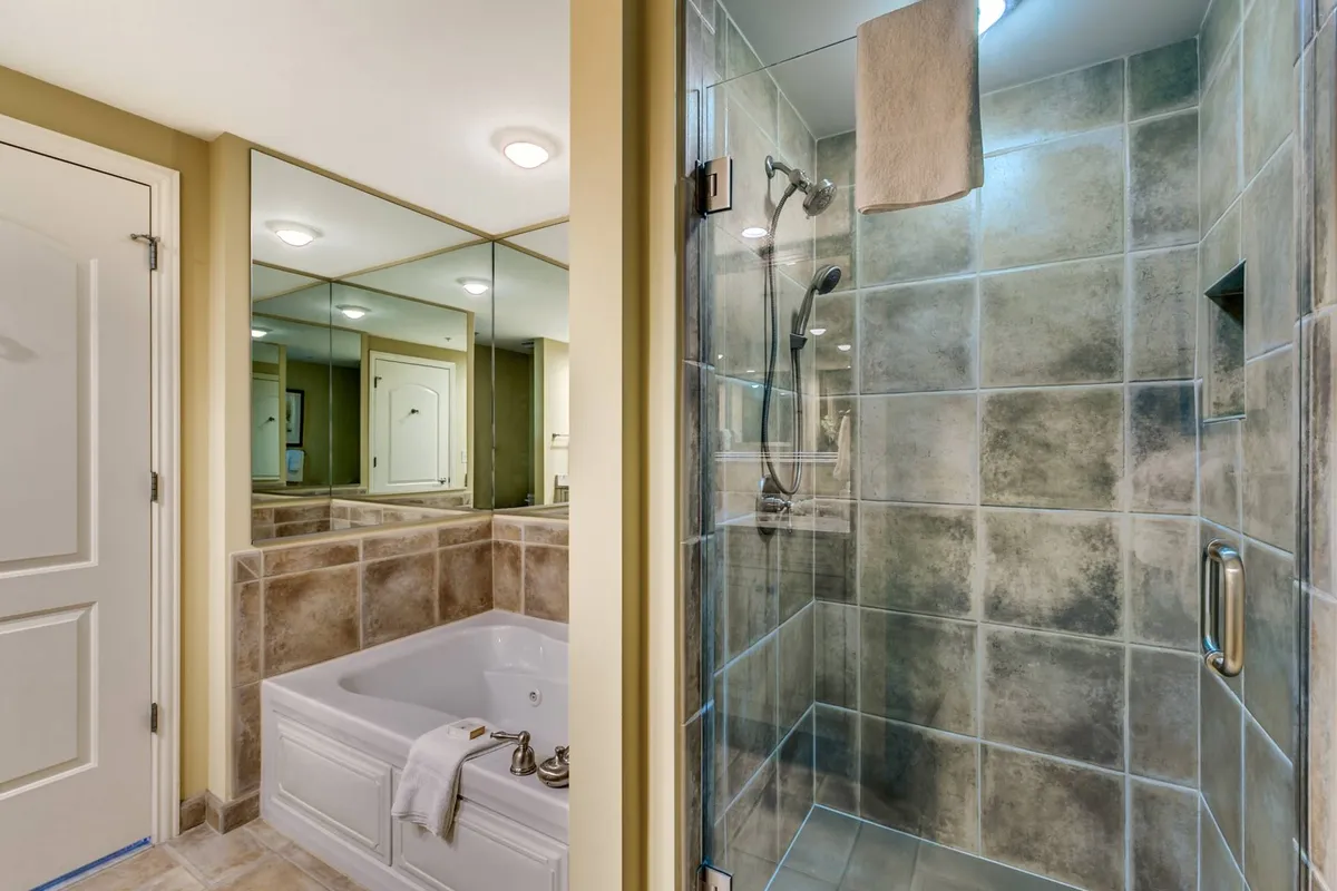 An interior image of a serene spa-like bathroom featuring a luxurious bathtub, a spacious shower area, and a mirrored wall. The tranquil setting hints at relaxing baths, self-care routines, and indulgence in spa treatments, mirroring the wellness facilities available on-site.
