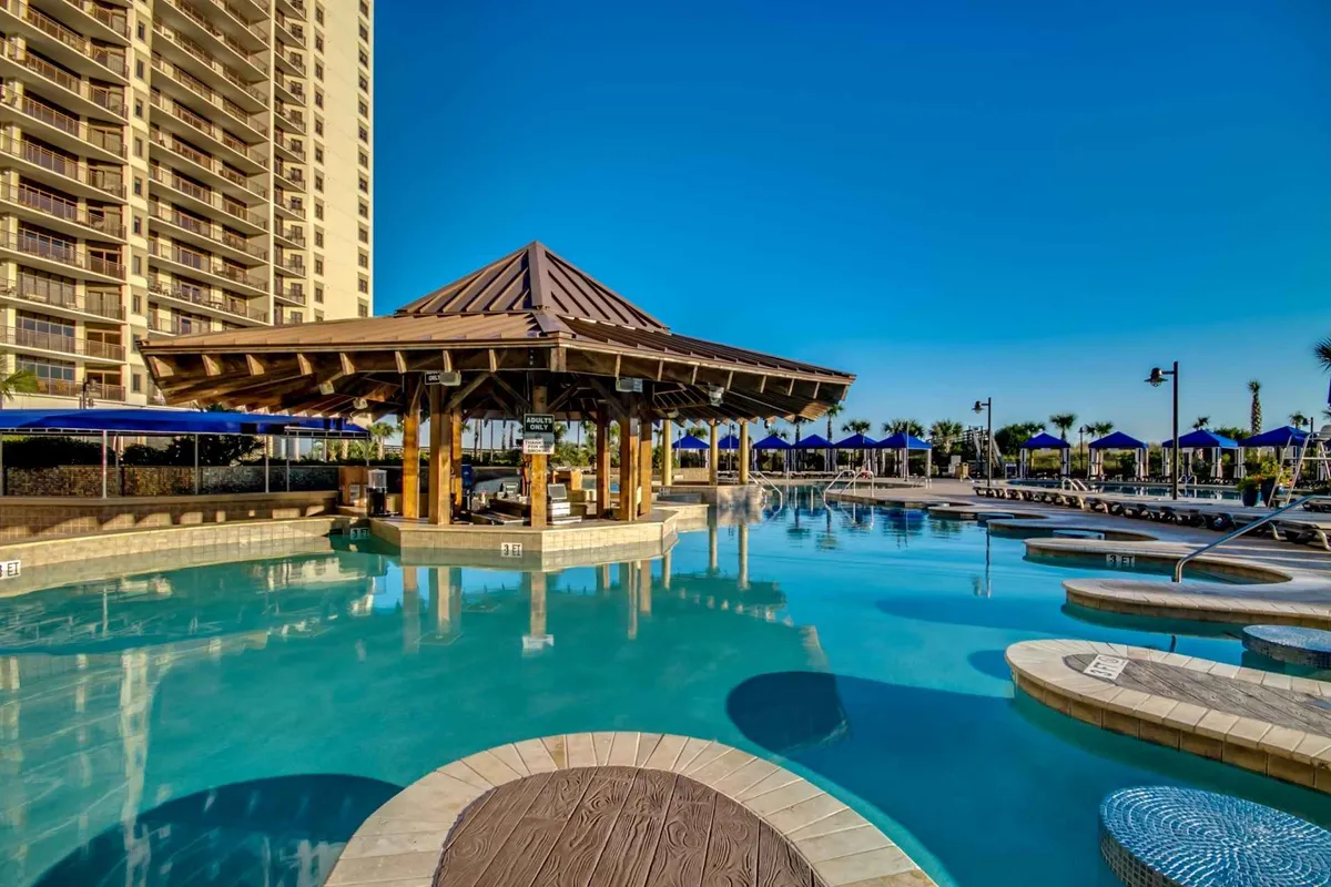 This image presents a vibrant pool area with a prominent swimming pool, an inviting gazebo, lounge chairs, and umbrellas. It shows guests enjoying swimming, sunbathing, and gathering for drinks at the poolside bar, while the setting sun adds a warm, welcoming glow.