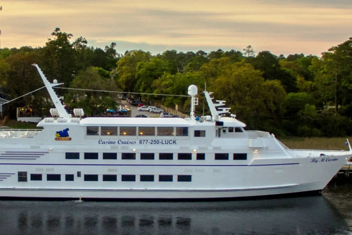 An exterior shot of a casino cruise ship set against lush trees and a tranquil waterway. The scene suggests opportunities for gaming, fine dining, and scenic excursions, all contributing to the area's lively and diverse entertainment scene.