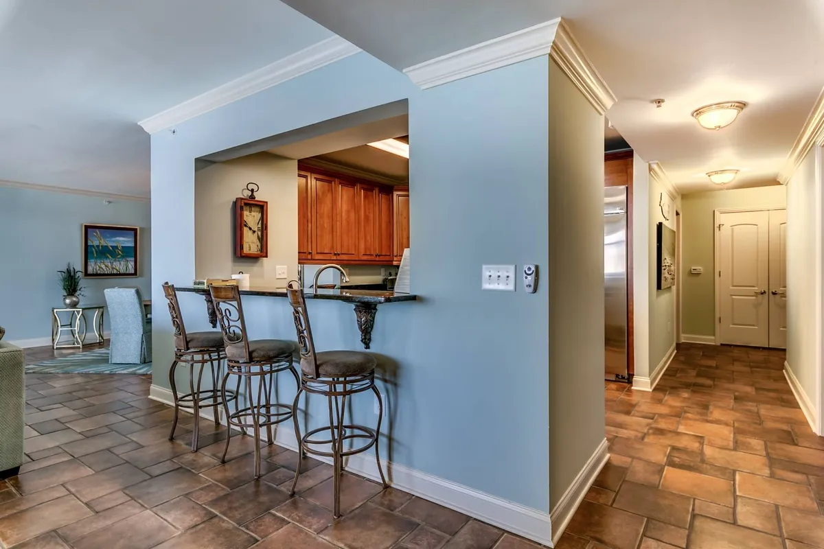 An inviting kitchen scene with bar stools at the counter, cabinetry, and stylish wall art. The space exudes a social, family-friendly vibe, encouraging casual conversations and group meals. The presence of seating and open counters connects kitchen prep to group dining and entertaining.